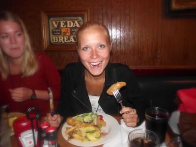 Sofia Westerholm sitter vid ett matbord med kniv och gaffel i händerna. Gaffeln i stucken i en matbit som hon håller framför munnen medan hon ler stort mot kameran.