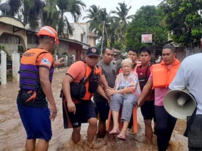 En kvinna bärs av räddningsarbetare, gatorna svämmar över av vatten.
