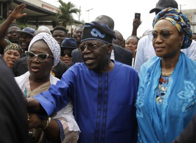 Bola Tinubu, en man klädd i blått med blå hatt, omringad av människor.