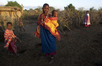 Kvinna som bär på barn i stepplandskap i kenya.