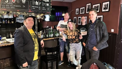 Fyran ,män och en kvinna poserar i en pub vid bardisken.