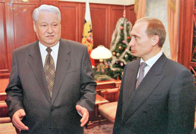 Jeltsin talar och Putin lyssnar. Männen bär mörkgrå kostymer. Jeltsins slips har ett rutmönster, Putins slips har ett prickmönster. I bakgrunden syns en julgran och den ryska flaggan.