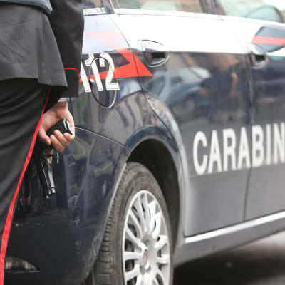 En italiens carabinieripolis håller i ett vapen bakom en polisbil.