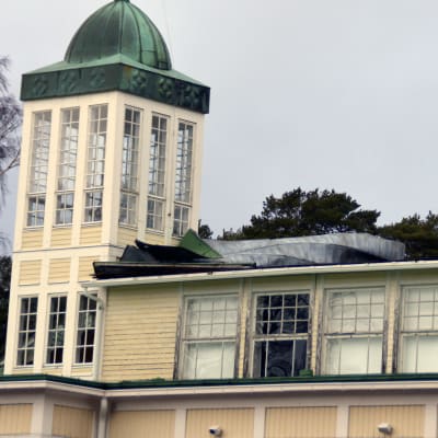 En gammal byggnad där en del av plåttaket har blåst bort.