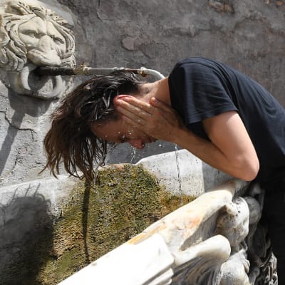 Någon skvättar vatten på sig vid en drickfontän i Rom i Italien.