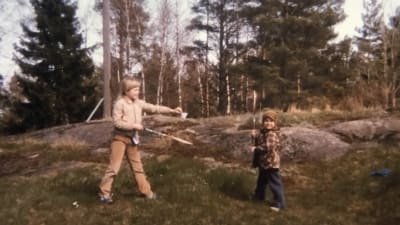 Heli Laaksonen Outi-siskonsa kanssa Taivassalossa noin vuonna 1980. Heli opettaa siskolle sulkapalloa. Helin asussa ruskean ja beigen yhdistelmä.