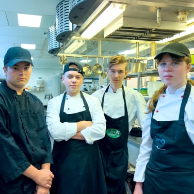Fyra ungdomar med förkläden står i ett kök.