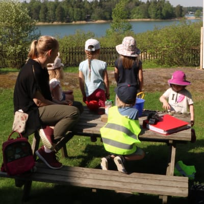 Amelie Lund, föreståndare på daghemmet Tallbo sitter utomhus runt ett bord med daghemsbarn.