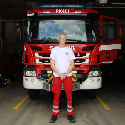 Palomies-ensihoitaja Sami Ruokolainen seisoo paloauton edessä Nurmeksen paloaseman kalustohallissa.