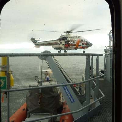 Helikopter kommer för att lämna över den nödställde till Sjöbevakningens fartyg.