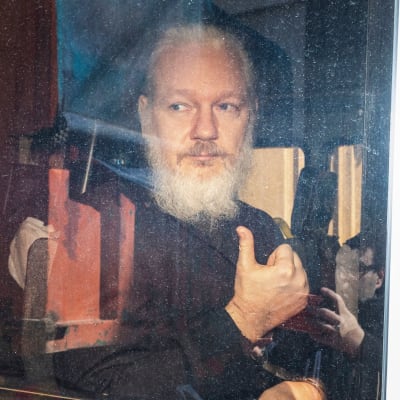 En skäggig Julian Assange fotograferad genom ett bilfönster. 