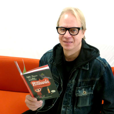Författaren Peter Sandström sitter i en röd soffa och håller i sin bok Rööluuvån.
