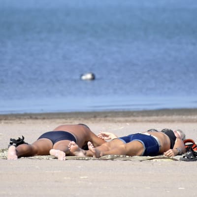 Två personer solbadar på en sandstrand.