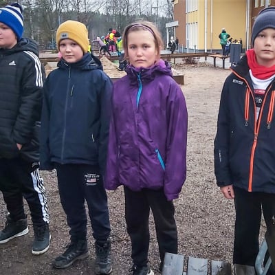 Fyra skolelever poserar på en skolgård.