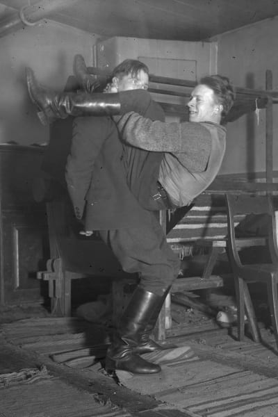 Två män leker leken "prova nacken", där den ena ska lyfta upp den ena med bara sin nackes styrka. Bilden är tagen 1935 i Bromarf.