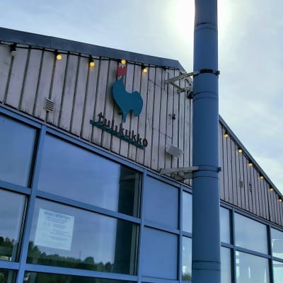 Kuva kahvila-ravintola Tulikukon julkisivusta. Ravintolan logo, vihreä kukko, näkyy kuvassa. Taustalla sininen taivas. 