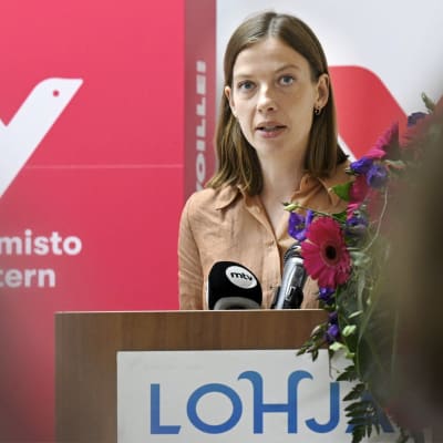 Li Andersson står i en talarstol och håller tal. Bakom henne syns Vänsterförbundets logotyp och på talarstolen står det Lohja (Lojo).