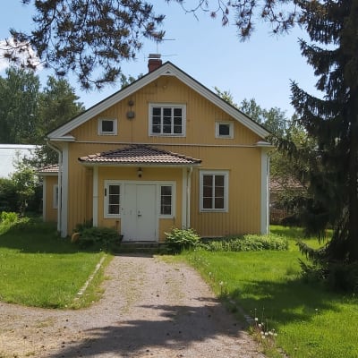Gult trähus med trädgård på sommaren.