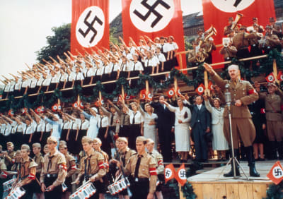 Kansaa ja univormupukuisia natseja tekemässä Hitler-tervehdystä juhlaparaatissa, taustalla suuria natsi-Saksan lippuja. Kuva elokuvasta Peltirumpu.