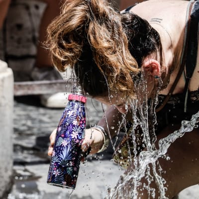 Henkilö viilentää itseää kastelemalla hiuksensa suihkulähteellä Roomassa.