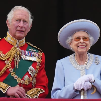 Prins Charles i röd uniformsjacka med många ordnar och drottning Elizabeth II i ljusblå hatt och dräkt.