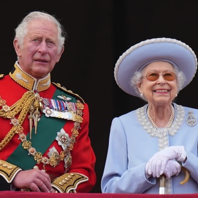 Prins Charles i röd uniformsjacka med många ordnar och drottning Elizabeth II i ljusblå hatt och dräkt.