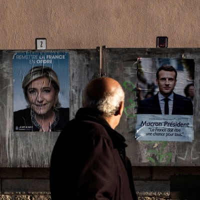 Äldre man tittar på valplakat för Marine Le Pen och Emmanuel Macron.