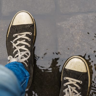 Ett par jeansklädda ben och sneakers syns av en person som går i en vattenpöl.