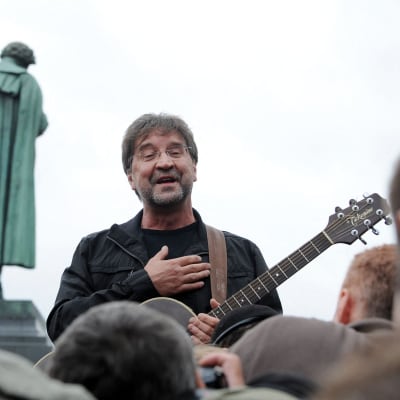 Jurij Sjevtjuk med en gitarr. I förgrunden publikens huvuden och i bakgrunden en staty.