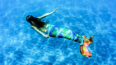 En sjöjungfru vars nedre del är stickad simmar i klarblått vatten.