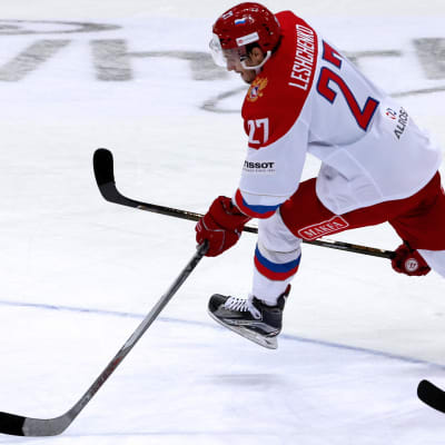 Vitklädd rysk ishockeyspelare rymmer undan med pucken från en tjeckisk motspelare