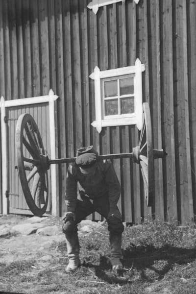 En man lyfter två kärrhjul på sina axlar utan att hålla i med händerna. Bilden är tagen 1932 i Esse.