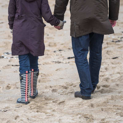 Man och kvinna går på stranden, håller varandra i handen