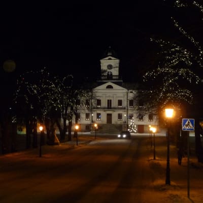 Julbelysning pryder ljusen längs med en gata i Kristinestad. I bakgrunden syns ett vitt stort hus.