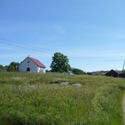 En skärgårdsby med en väg genom en äng och en vit kyrka i bakgrunden