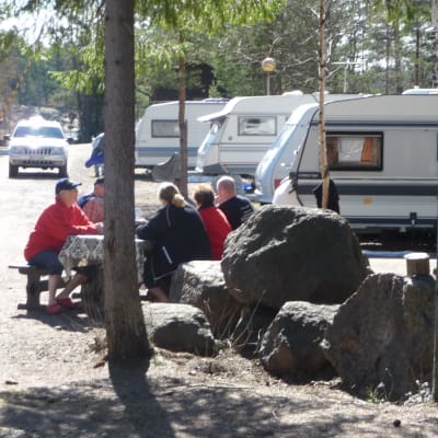 Husvagnar vid en camping och en grupp människor som diskuterar.