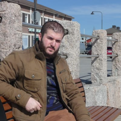Amir sitter på en bänk i Kristinestad en solig vårdag.