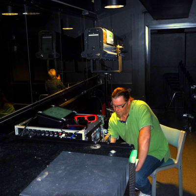 Janne Lindgård, en man med glasögon och grön t-skjorta, sitter vid en filmprojektor i ett nästan helt mörkt rum.