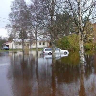 Bil på översvämmad parkeringsplats invid höghus.