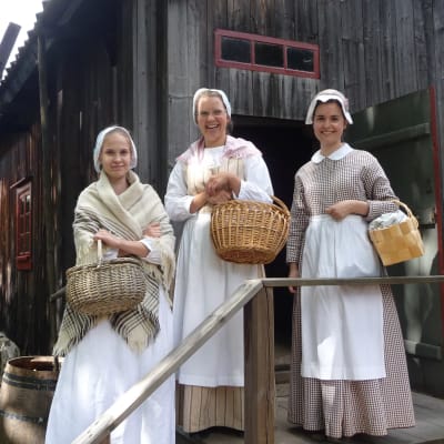Tre kvinnor står utanför en museistuga på Klosterbacken. 
