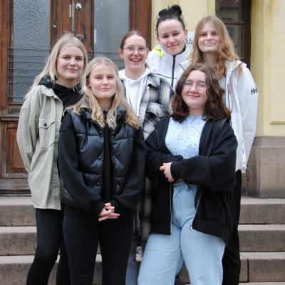 Grupp med unga kvinnor står på en stentrappa utanför gammalt hus.