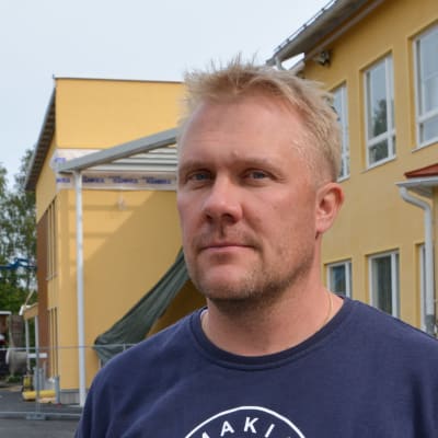 man i blå tröja framför gul skola