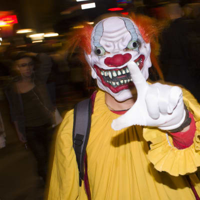 En person utklädd till en skrämmnade clown. Gul dräkt, rött hår och förvridet ansikte.