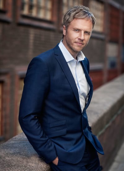 Författaren och den menatal tränaren Olof Röhlander poserar i blå kostym och vit skjorta.
