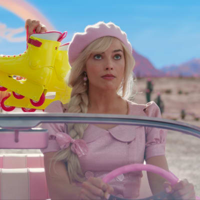 Auton takapenkillä istuva Ken esittelee rullaluistimilla auton ratissa olevalle Barbielle.