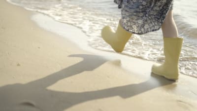 barnfötter i gula stövlar går på strand