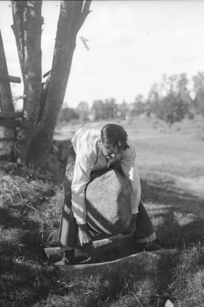 En man lyfter en stor sten med sina armar. Bilden är tagen 1932 i Terjärv, Risbacka.