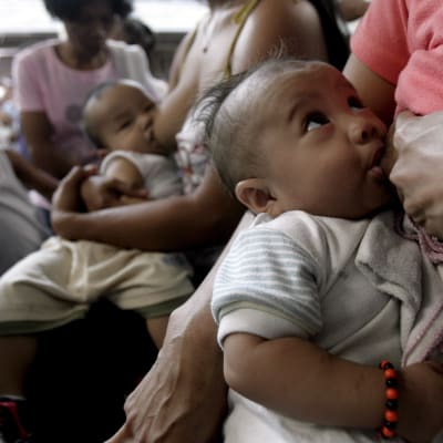 En baby tittar upp mot sin mamma samtidigt som babyn blir ammad. Filippinska mammor samlas i Manila för att amma sina barn.