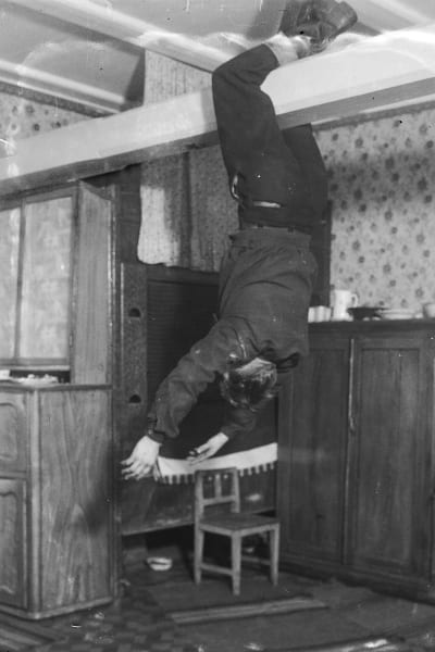En man hänger i sina ben från takåsen. Bilden är tagen 1937 i Korsnäs, Harrström.
