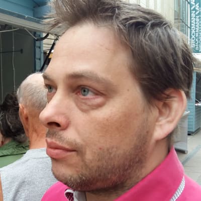 Jyrki Åland, en man med skäggstubb och anilinröd skjorta.